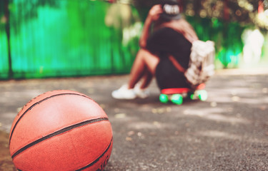 Closeup photo basketball ball with girl sitting on plastic orange penny shortboard on asphalt