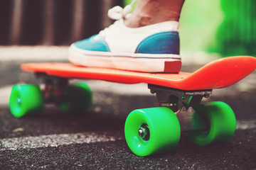 Close up of feet of girl sneakers rides on orange penny skateboard on asphalt