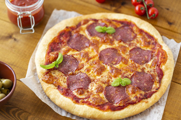 Rustic pizza with salami, mozzarella, olives and basil.