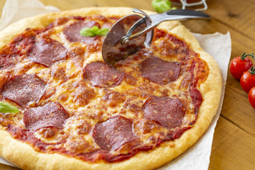 Rustic pizza with salami, mozzarella, olives and basil.