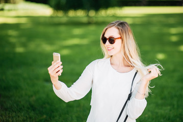 Portrait of a young woman in glasses enjoying a smartphone in the park. Beautiful sunny day.