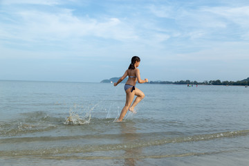 Teenage wearing bikini running at the beach by the sea.