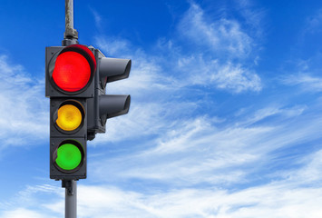 Red semaphore light with yellow and green and cloudy sky background