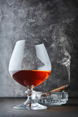 Strong alcoholic drink cognac in sniffer glass with smoking cigar in crystal ashtray