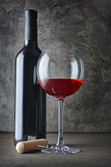 Red wine bottle and glass for tasting with corkscrew in dark cellar