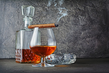 Strong alcoholic drink cognac in sniffer glass and decanter with smoking cigar and crystal ashtray