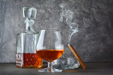 Strong alcoholic drink cognac in sniffer glass and decanter with smoking cigar in ashtray
