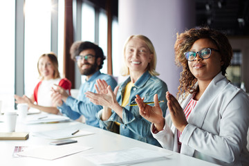 Happy intercultural colleagues clapping their hands after speech of colleague at seminar or conference