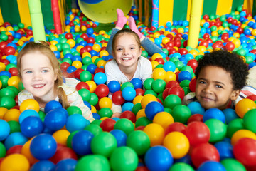 Fototapeta na wymiar Colorful portrait of three happy kids smiling happily at camera while having fun in ball pit of children play center, copy space