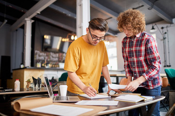 Two young men discussing working points while making plan for new week at meeting