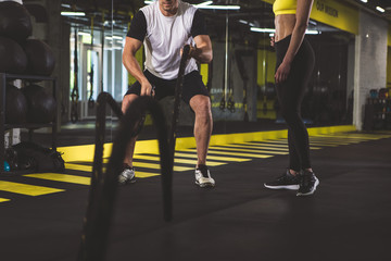 Male doing physical exercise with equipment while situating near girl in gym. Sport concept