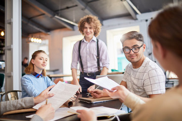 One of managers taking paper from hand of colleague while planning work or making notes at meeting