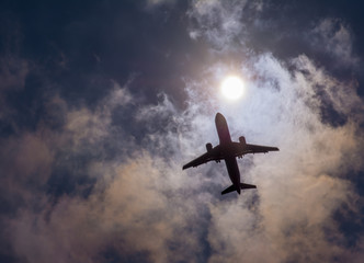 The plane flies in the sky against the sun.
