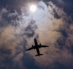 The plane flies in the sky against the sun.
