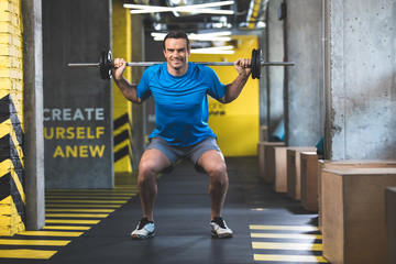 Fototapeta na wymiar Full length portrait of beaming man keeping sport equipment while doing workout in fitness center