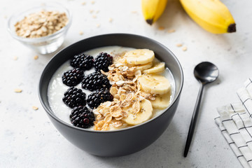 Breakfast smoothie bowl with banana, granola and blackberry on grey concrete background, closeup view, selective focus