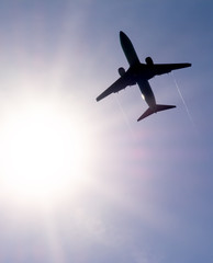 The plane flies in the sky against the sun.
