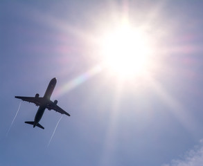 The plane flies in the sky against the sun.

