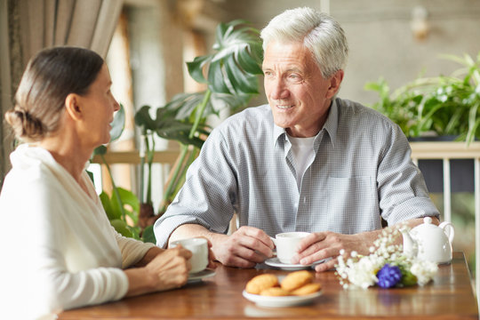 Senior grey-haired man and his wife having tea in cafe and talking