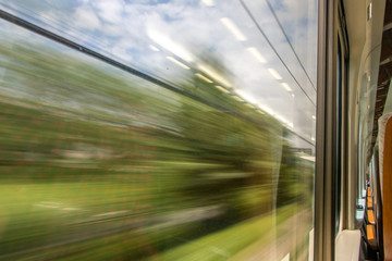 a view out from the window of a train. The green nature is running behind the windows of a traveling train