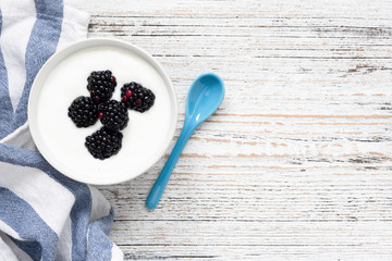 Yogurt with berries in bowl on wooden background. Top view, copy space for text