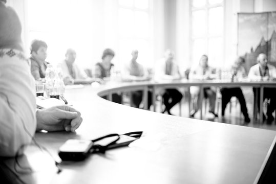 People At A Round Table Discuss Different Issues. B/W Photo. The Photaography Is Blurry