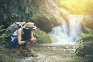 Young hiking lady washing her hands in the fresh cool water of a mountain stream.