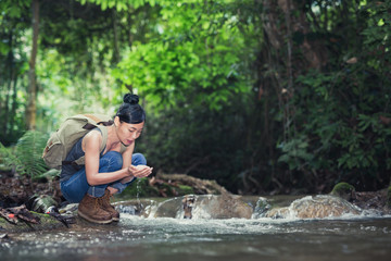 Young hiking lady washing her hands in the fresh cool water of a mountain stream.