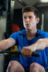 Fototapeta premium Man In Gym Exercising On Rowing Machine