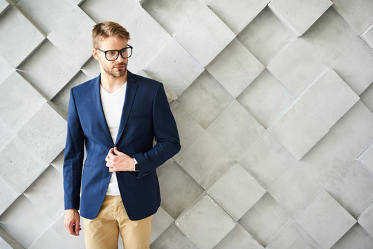 Waist Up Portrait Of Male Standing And Touching Jacket. He Is Wearing Eyeglasses And Looking Sideways Confidently. Copy Space In Right Side