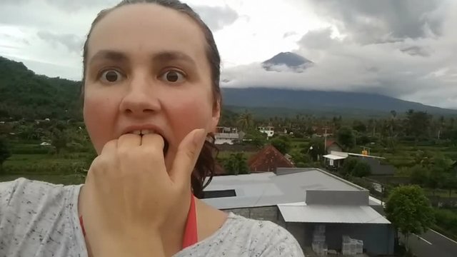 woman making selfie on cell phone, making scared face, agung Volcano erupting january 2018
