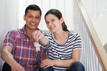 Obraz premium Young Couple Sitting On Stairs Holding Keys To New Home
