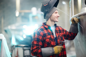 Young welder in workwear and protective mask repairing motorboat or ship
