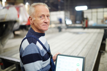 Senior worker of shipyard looking at camera by workplace during working process