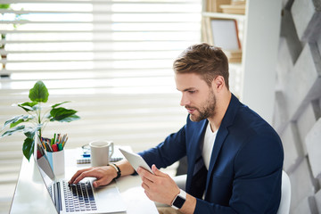 Side view profile of attentive man sitting at desktop. There are laptop, pens and notebook with...