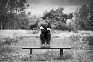 Eine anonyme einsame traurige Frau sitzt allein auf einer Bank mit verschränkten Armen. Monochromes Porträt - obrazy, fototapety, plakaty