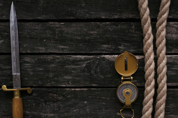 Moorings rope, dagger blade and compass on aged timber background.