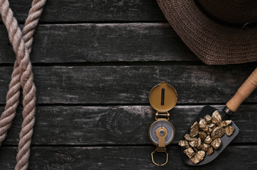 Tourist hat, shovel full of gold ore, compass, rope on aged wooden table background. Treasure hunter concept. Adventurer accessories.