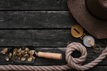 Tourist hat, shovel full of gold ore, compass, rope on aged wooden table background. Treasure hunter concept. Adventurer accessories.