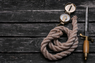 Dagger blade, moorings rope and compass on vintage wooden background with copy space. Adventurer...