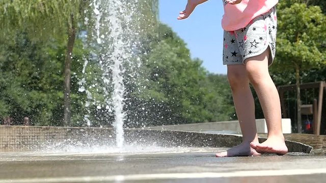 Slow motion. Barefoot girl legs play with fountain water jets. Summertime enjoyment. 