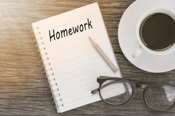 Education concept. Homework word on notebook with glasses, pencil and coffee cup on wooden table.