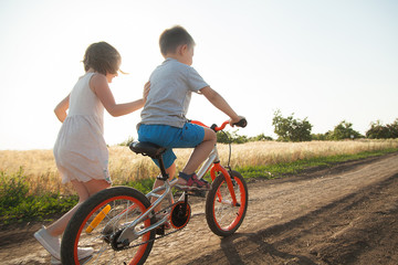  A boy and a girl ride a bicycle in the summer field
