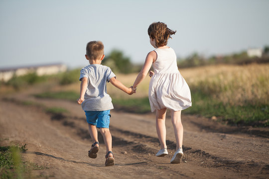  A boy and girl holding hands amicably running across the field in the summer