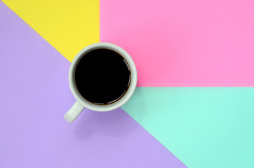 Small white coffee cup on texture background of fashion pastel blue, yellow, violet and pink colors paper in minimal concept