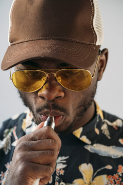 Black stylish man wearing sunglasses. He is vaping with an electronic cigarrete outdoor