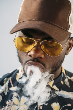 Black stylish man wearing sunglasses. He is vaping with an electronic cigarrete outdoor