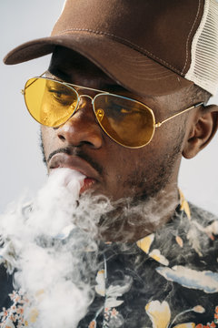 Black stylish man wearing sunglasses. He is vaping with an electronic cigarrete outdoor