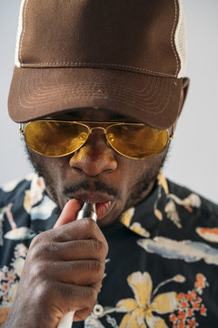 Black stylish man wearing sunglasses. He is vaping with an electronic cigarrete outdoor