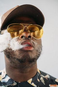 Black stylish man wearing sunglasses. He is vaping with an electronic cigarrete outdoor